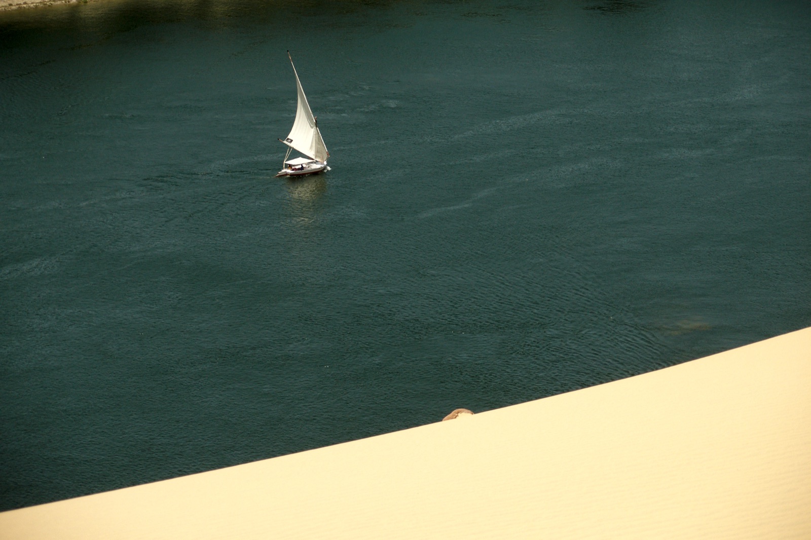 A white felucca sail rising above the Nile at Aswan between rocky banks
